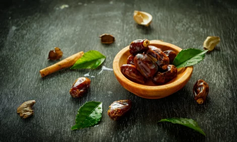A wooden bowl full of dates, with dates and dates leaves strewn alongside.