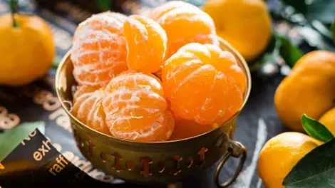 Peeled oranges in a carved golden bowl, surrounded by unpeeled oranges.
