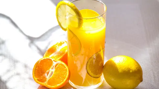 A glass of orange juice near a lemon and a sliced orange.