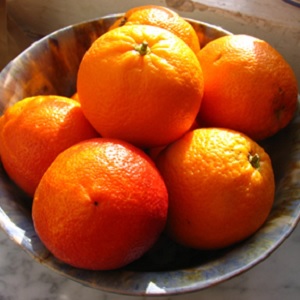 A bowl of oranges in a silver bowl, illuminated by evening light.