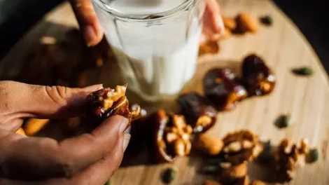 A person holding a half-eaten stuffed date and a glass of milk.