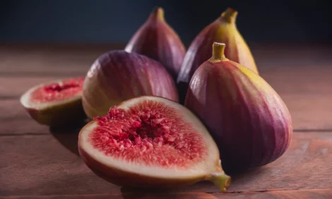 Whole and cut fig fruit sitting on a wooden surface.