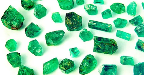 A large collection of raw, pure Emerald shards ranging in caret and clarity resting on a white surface to display the opacity and impurities. Dennis Harper Emerald Sept 2012 parcel 4285 apsm (CC BY ND 2.0)| Emerald Metaphysical Properties and Meaning.