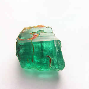 A semi-clear, brilliant 8.1 caret emerald chunk with an auburn golden inclusion well lit and resting atop a white surface to better clearly see the impurities and inclusions. Dennis Harper Emeralld01 olyp 810ct 4247ap (CC BY-ND 2.0) | Emerald Metaphysical Properties and Meaning |