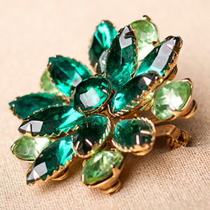 A series of small emeralds cut into petals and set into gold to form a beautiful emerald flower brooch resting on a tan fabric jewelry holder. Seattle Goodwill Emerald Flower ( CC BY 2.0 ) | Emerald Metaphysical Properties and Meaning | 