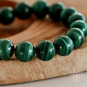 A bracelet of smoothed shiny Malachite beads with a banded pattern resting atop a cross-section of tree rings. Hyperlinks to Conscious Items product "The Anti-Anxiety Bracelet" in a new tab.
