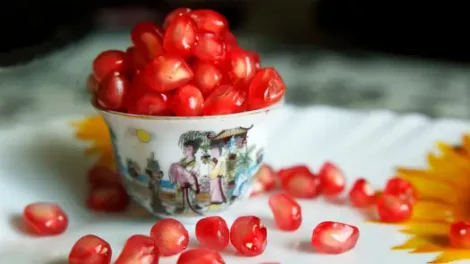 Pomegranate seeds overflowing from a decorative China cup.