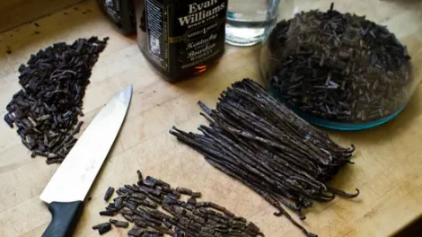 Vanilla beans, some cut and some uncut. A knife is in display as well as a bottle of Kentucky whiskey. A glass container of cut vanilla beans is nearby and this appears to be the setup to make vanilla extract.