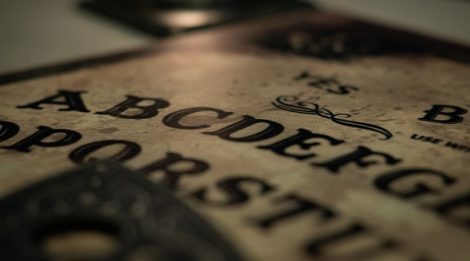 A close-up of a Ouija Board, lit by candlelight.