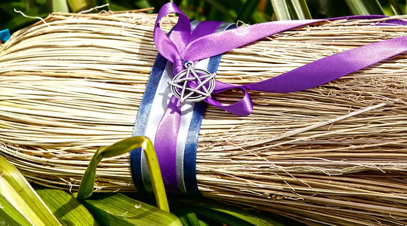 A besom brush tied with white, blue, yellow and purple ribbons and decorated with a pentacle.