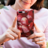 Woman in a pink shirt holding an iPhone 8 Plus with our Pomegranate Seeds iPhone 8 Plus Case.