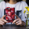 A woman with a silver ring on her finger holding an iPhone 8 Plus with a Pomegranate Seeds iPhone case.