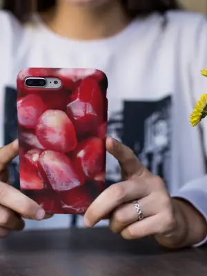 A woman with a silver ring on her finger holding an iPhone 8 Plus with a Pomegranate Seeds iPhone case.