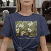 A woman wearing a navy-colored t-shirt with a vanilla orchid graphic. Text on the bottom of the vanilla orchid graphic says: "Vanilla Phalaenopsis."