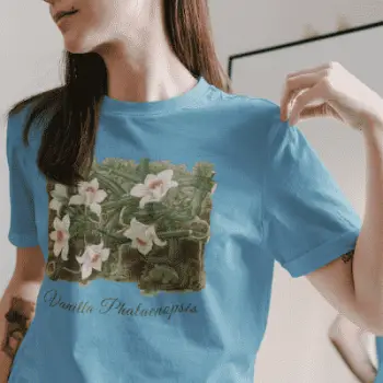 A woman wearing a ocean blue gray t-shirt with a vanilla orchid graphic. Text on the bottom of the vanilla orchid graphic says: "Vanilla Phalaenopsis."