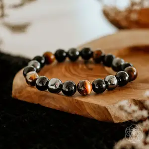 A bracelet with hematite, tiger's eye and black obsidian beads from Conscious Items sitting on a wooden slab.
