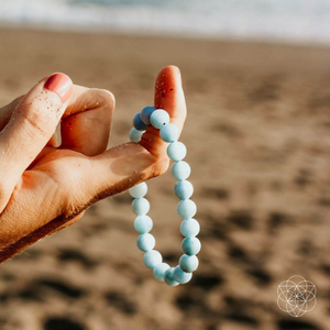 A woman holding an Aquamarine Soothing Bracelet from Conscious Items at the beach.