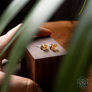 A pair of citrine earrings from Conscious Items, sitting on a wooden block with leaves decorating the foreground.