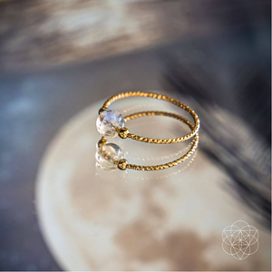 A moonstone ring from Conscious Items with a 14k gold band, resting on a glass surface.