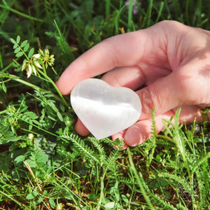 A person holding the Selenite Harmonious Heart Sphere from Conscious Items over grass.