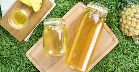 Two glass jars of pineapple vinegar sitting on a cutting board in the grass.
