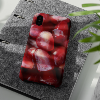 An iPhone XR near a plant on a gray book, decorated with our Pomegranate Seeds iPhone Case.