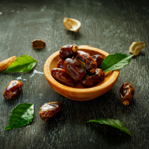 A wooden bowl full of dates, with dates and dates leaves strewn alongside.