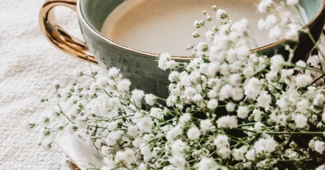 White Baby's Breath flowers resting next to a cup of blonde coffee.