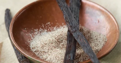 Vanilla sugar in a wooden bowl, with two vanilla beans laid out across the top of the bowl.
