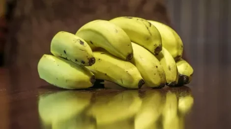 A bunch of yellow bananas sitting on a glossy wooden surface.