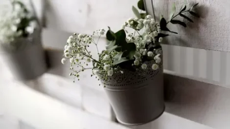 White baby's breath flowers in a decorative wedding vase hanging on a wall.