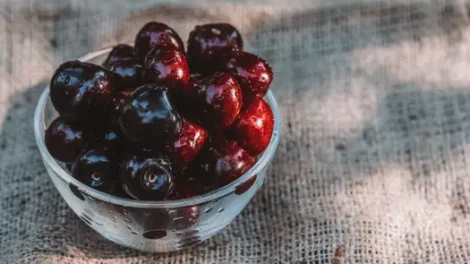 A bowl of moistened cherries in a clear bowl, resting on a woven mat.