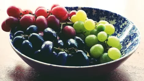 Red, purple and green grapes in a white ceramic bowl with a blue floral design.