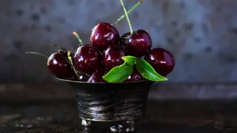 Moistened, deep-red cherries in a silver bowl.