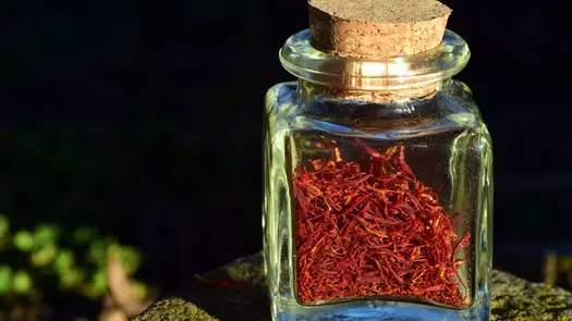 Saffron sprigs in a cork-sealed glass jar, sitting outside on a mossy stump.