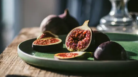 Sliced figs on a green platter sitting on a wooden table.