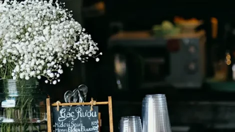White baby's breath flowers in a glass jar near a chalkboard menu and clear plastic cups.