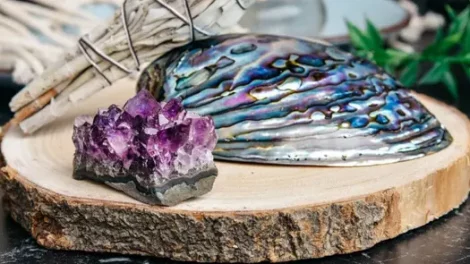 An amethyst geode, iridescent seashell, and sage smudge stick from Conscious Items on a wooden slab.
