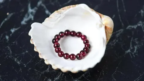 A garnet beaded ring sitting on a seashell.
