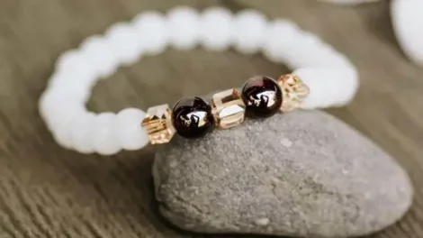 A bracelet with two red garnet stones and white and gold beads sitting on a rock.