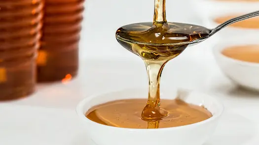 Honey being poured into a spoon then into a white bowl.