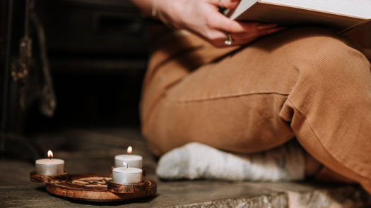 A woman sitting and reading a book next to burning candles on a pentacle candle holder.