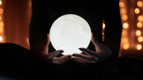 A person holding a glowing, moon-like orb.