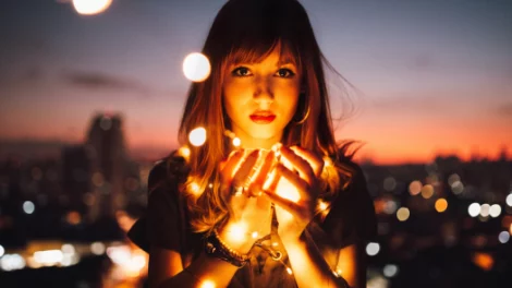 A woman holding bright lights that remind of fireflies, with her arms wrapped in bright lights.