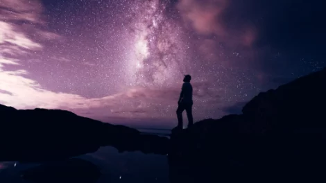 A man stands on a rooftop, looking out at the purple night sky.