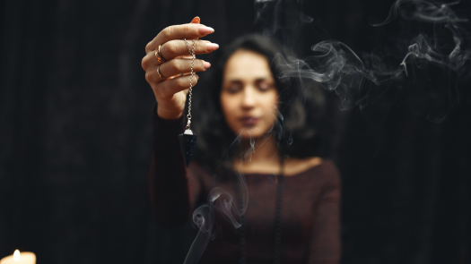 A woman holding a crystal pendant above smoke while meditating.
