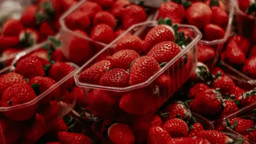 A crate filled with red strawberries. The strawberries are ripe and juicy, with a few green leaves still attached. The crate is made of a clear plastic, so the strawberries are visible from all sides.