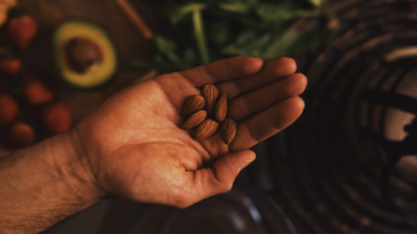 A person's hand holding a handful of raw almonds. The almonds are light brown and have a smooth texture.