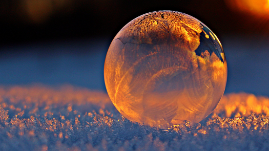 Ice bubble on snow glistening in sunset light.